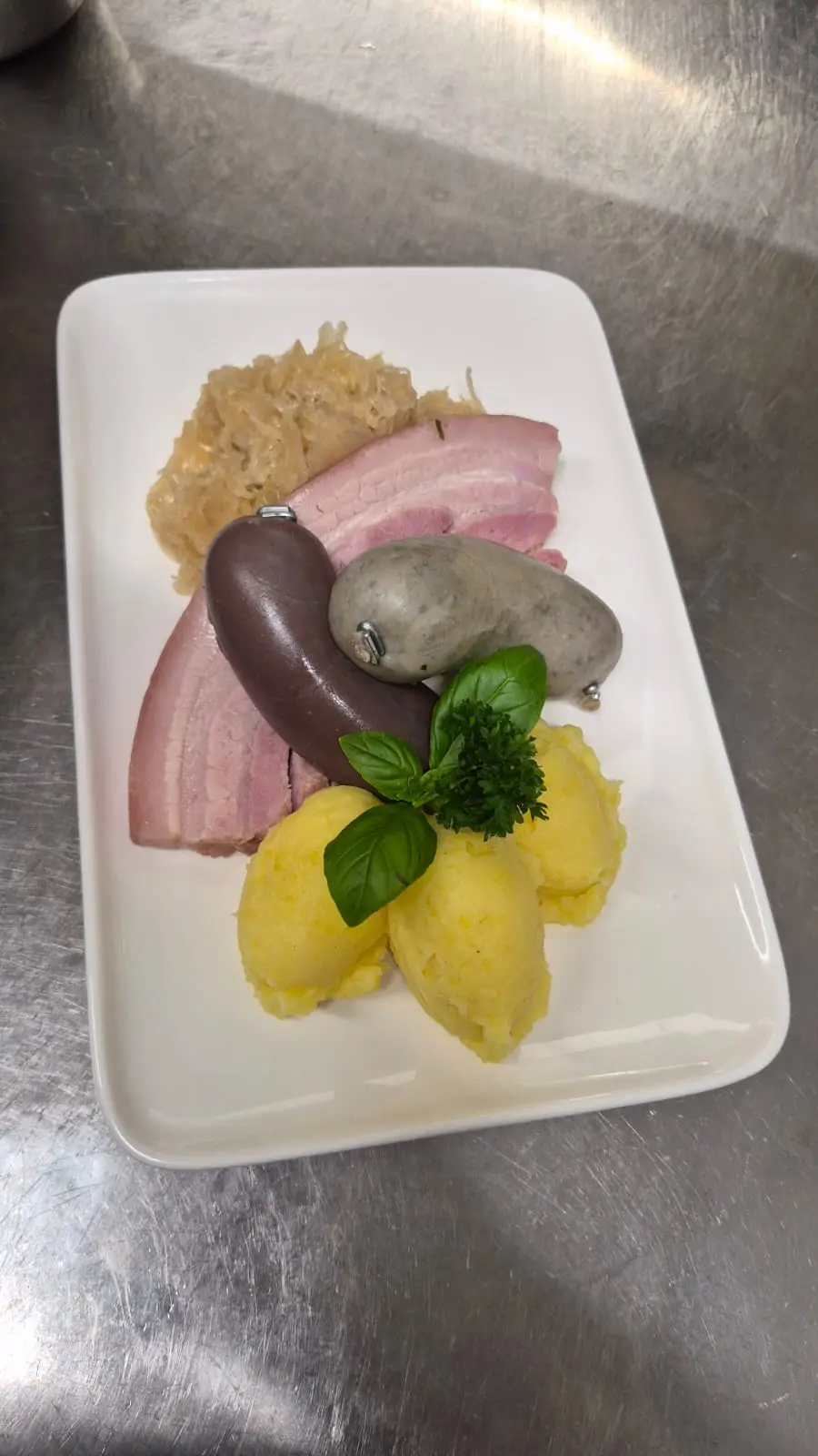 Schlachtplatte auf weißem Teller: Blut- und Leberwurst, Bauchfleisch, Sauerkraut und Kartoffelpüree