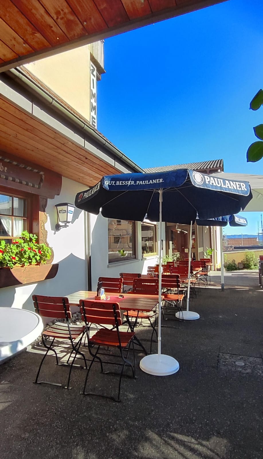 Biergarten-Bestuhlung mit Sonnenschirmen vor dem Haus