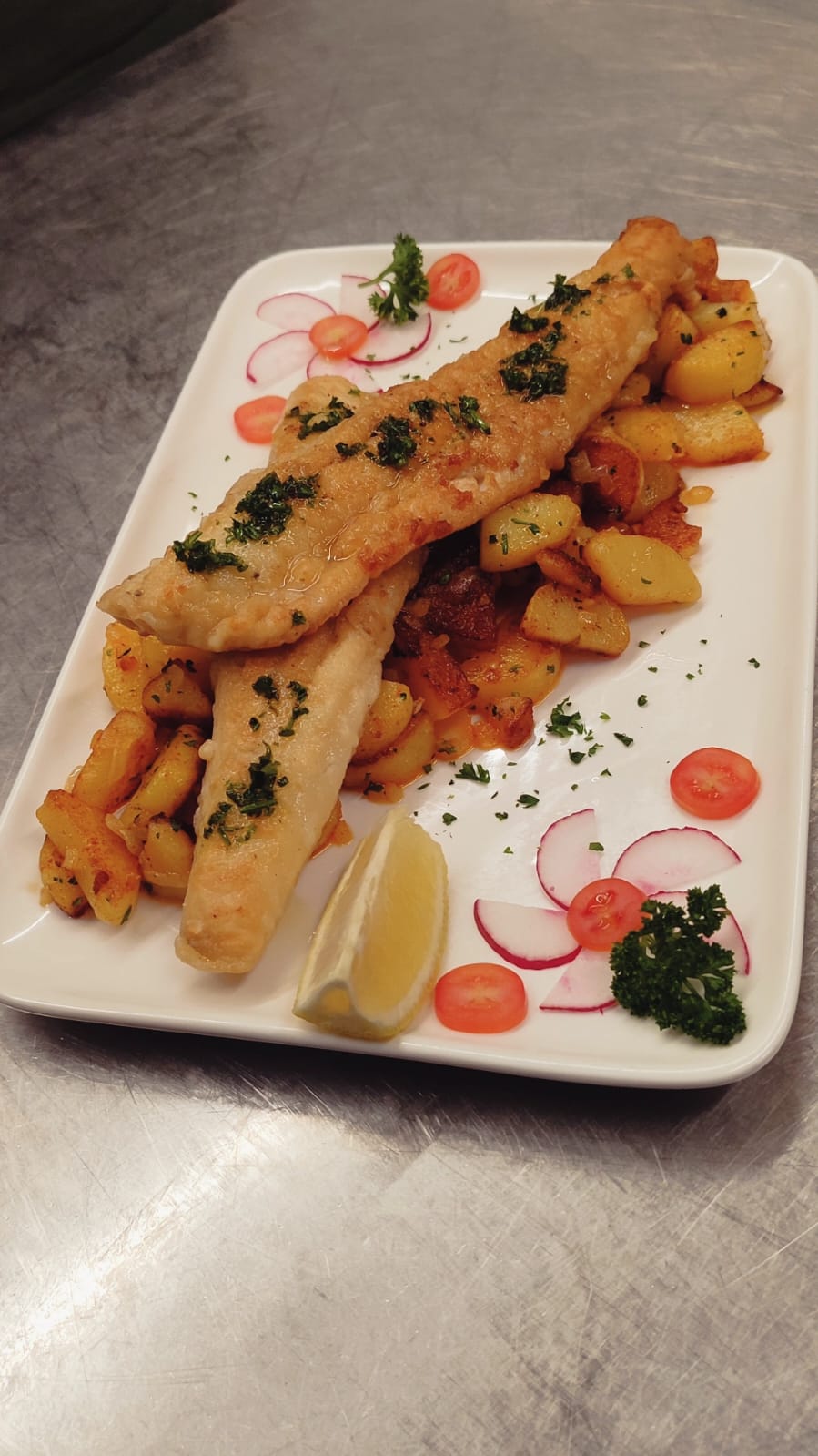 Gebratene Fischfilets mit Bratkartoffeln, angerichtet in der Küche